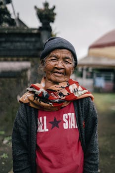 Portrait of a smiling elderly woman in Bali, showcasing the local culture with traditional architecture in the background.