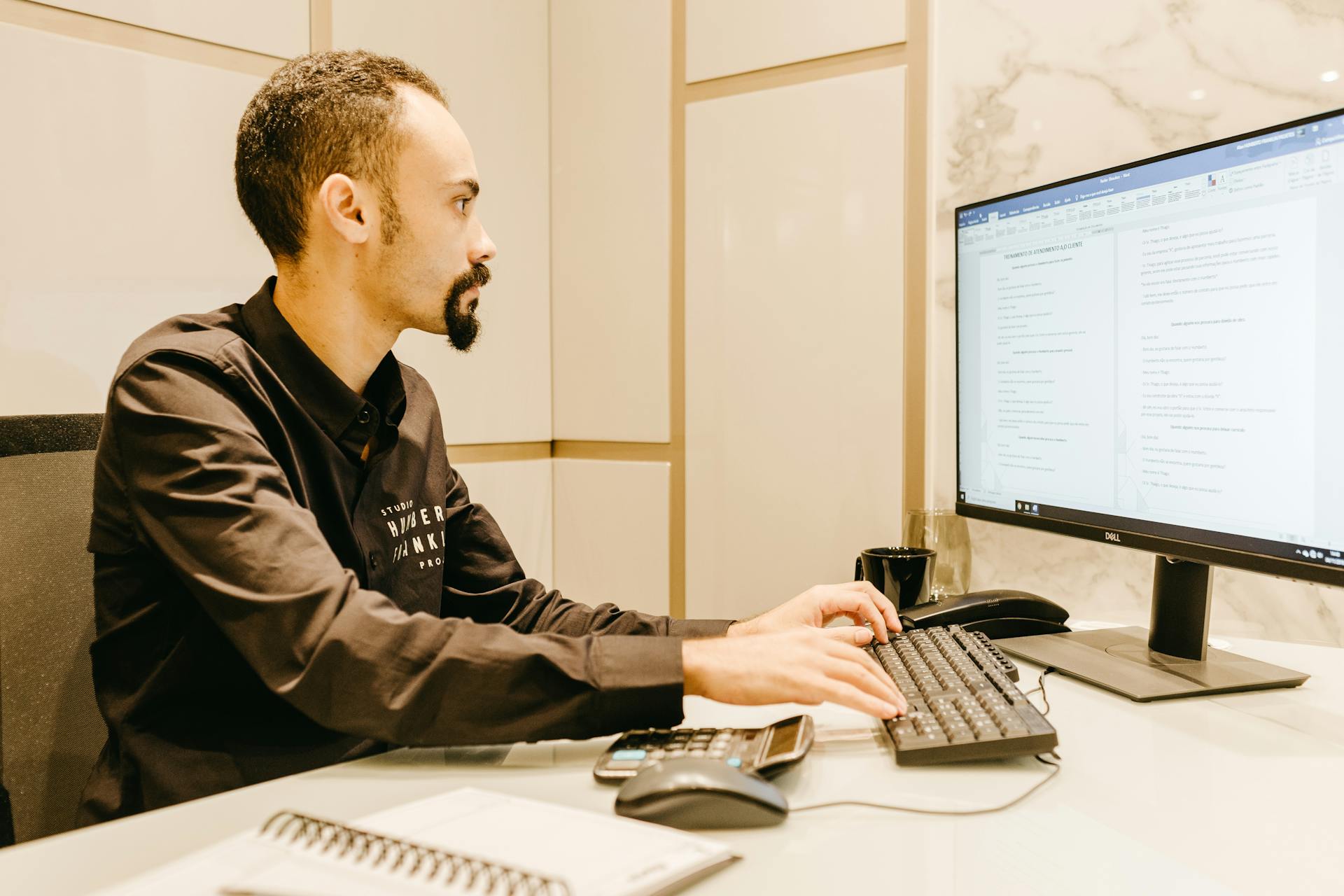 Young man focused on typing, working on computer in sleek, modern office.