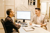 两名商人在时尚现代的办公桌前，使用电脑和笔记协作讨论工作