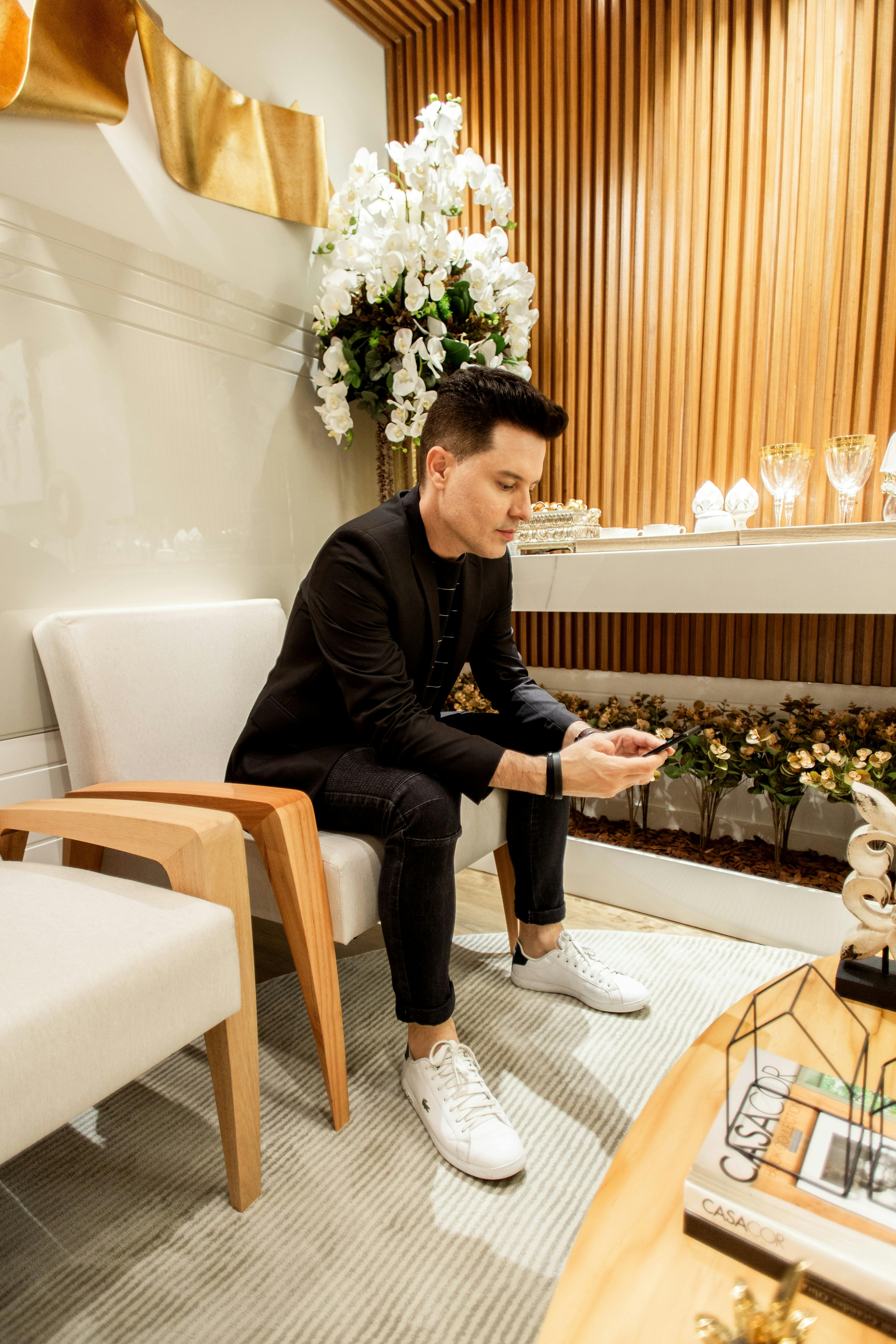一名男子坐在一间配有木制装饰和花卉布置的时尚现代房间里，正使用着智能手机