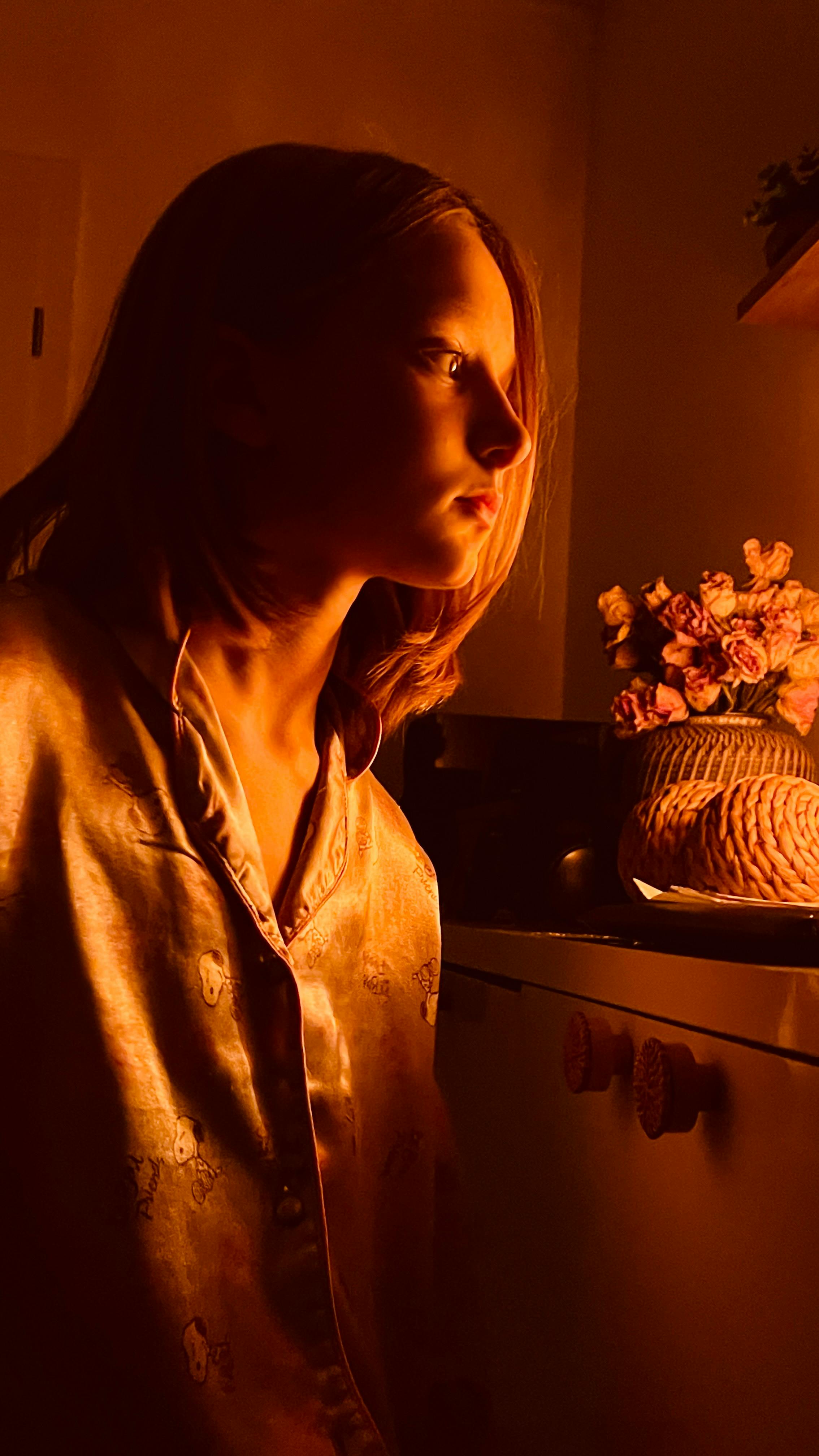 Moody portrait of a girl in warm, soft lighting indoors, next to flowers.
