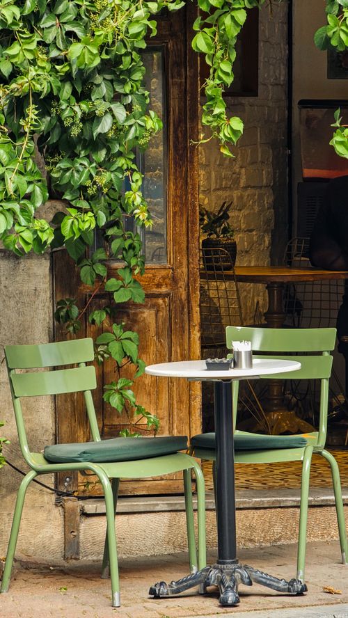 Free A quaint cafe setting with green chairs and lush foliage, ideal for a serene urban escape. Stock Photo