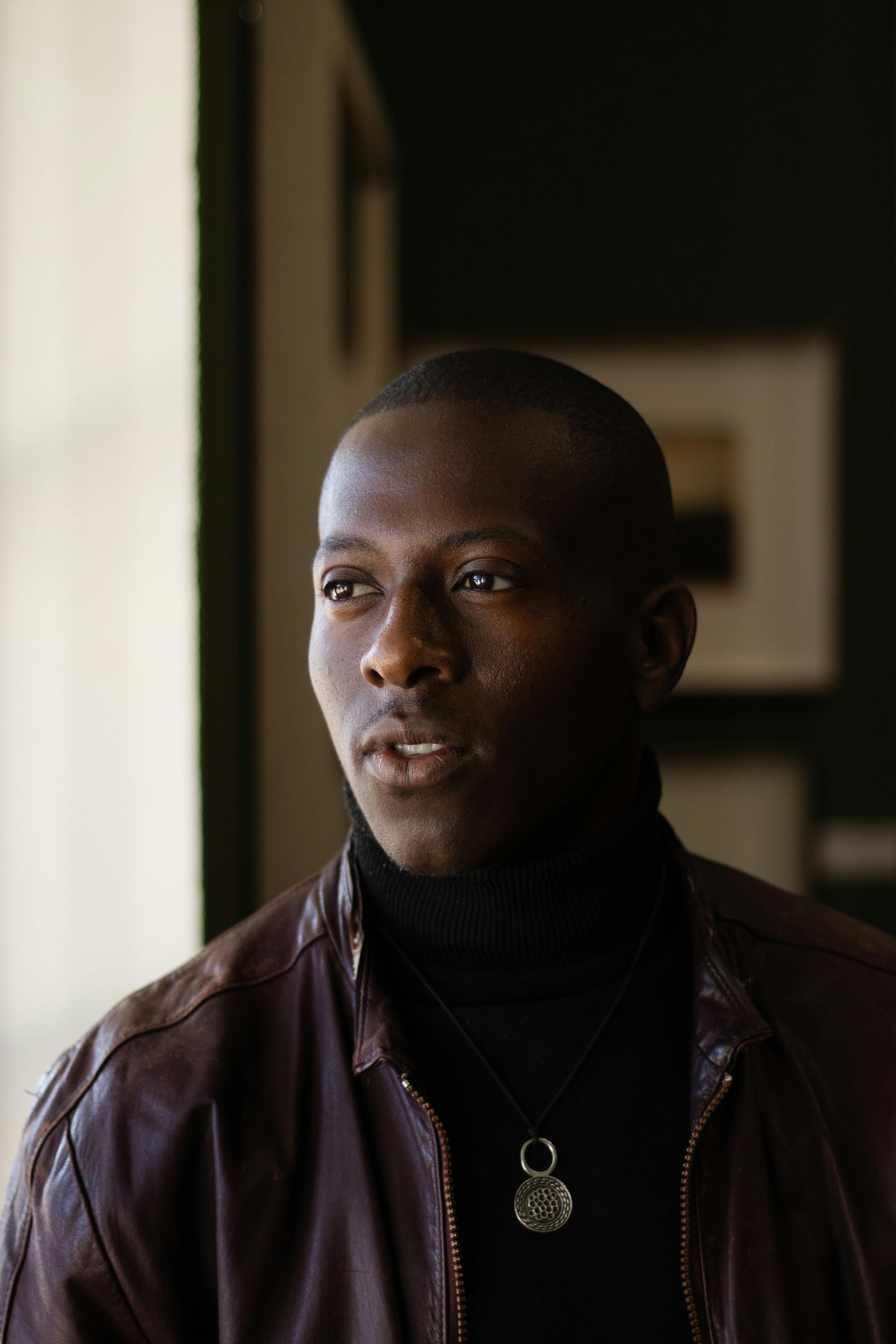 Thoughtful man in leather jacket gazing away in moody indoor setting.