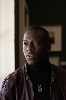 Thoughtful man in leather jacket gazing away in moody indoor setting.