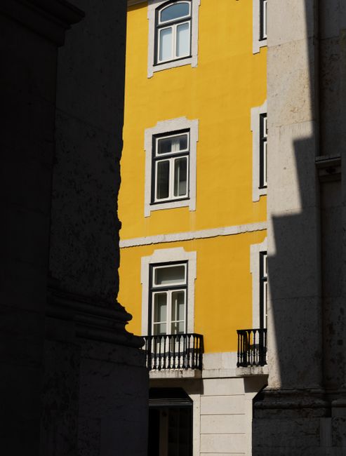 A vibrant yellow building facade lit by sunlight in Lisbon, Portugal's historic district.