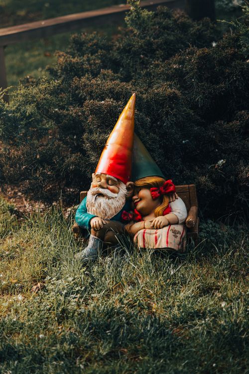 Free Colorful garden gnomes cozily resting on a bench amidst lush greenery, evoking tranquility. Stock Photo