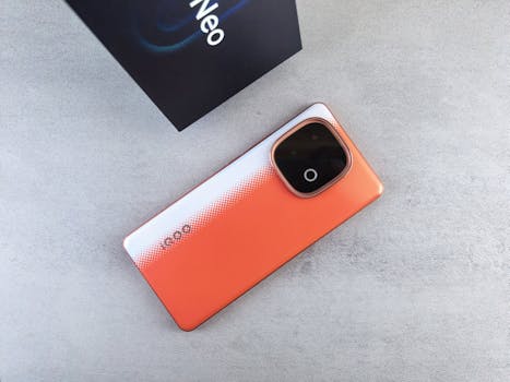 Orange smartphone with unique back design and its box on a textured surface, viewed from above.