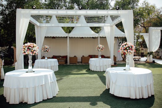 Charming outdoor wedding setup with white draped pergolas and floral centerpieces under a sunny sky.