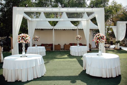 Free Charming outdoor wedding setup with white draped pergolas and floral centerpieces under a sunny sky. Stock Photo