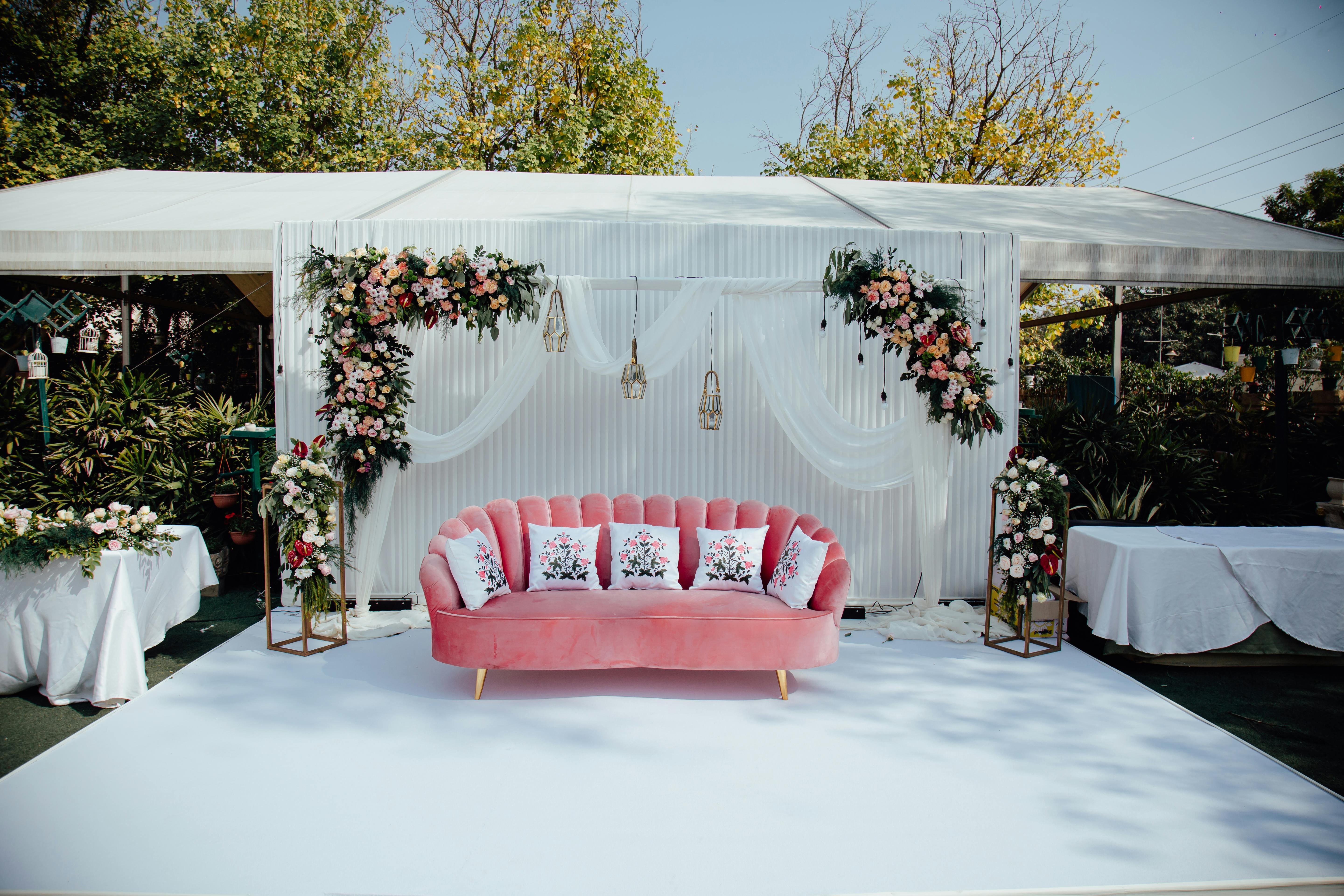 Outdoor wedding setup with floral arrangements, pink sofa, and elegant decor in Gurugram, India.