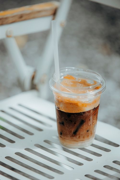 Free A refreshing iced coffee with a straw on a slatted white chair outdoors in daylight. Stock Photo