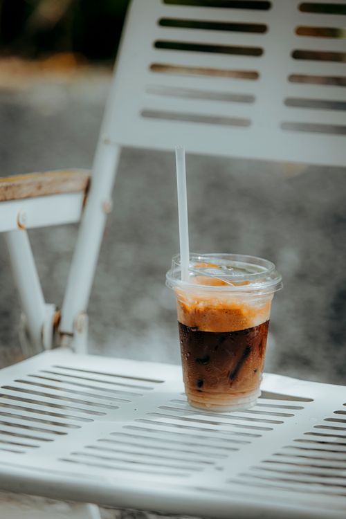 Free A refreshing iced coffee sits on a white chair outdoors, perfect for a sunny day. Stock Photo