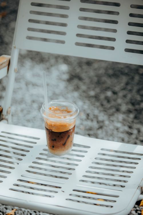 Free Chilled iced coffee in clear plastic cup placed on a metal chair outdoors. Stock Photo