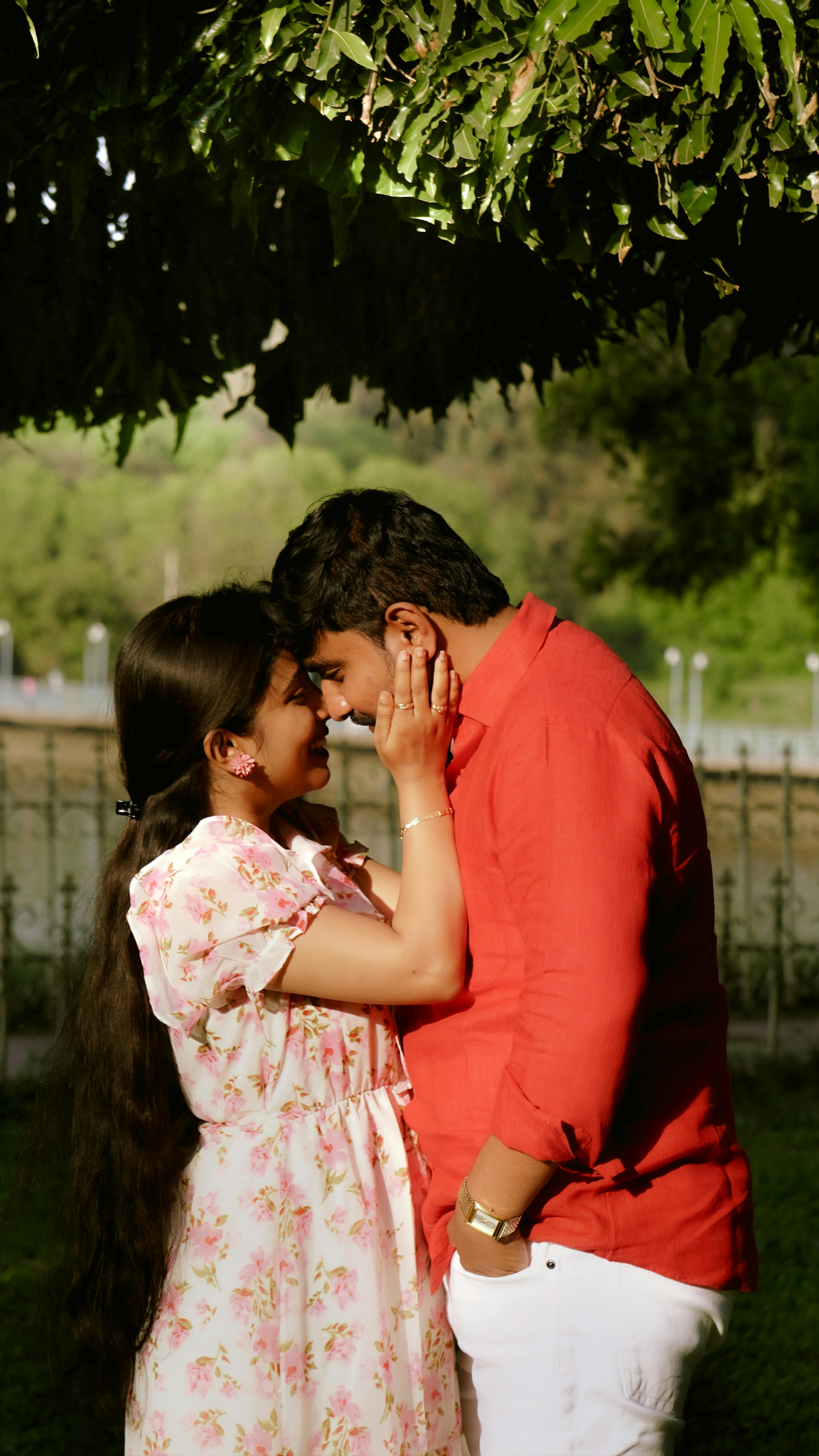 A loving couple shares a tender moment under leafy greenery in a serene park.