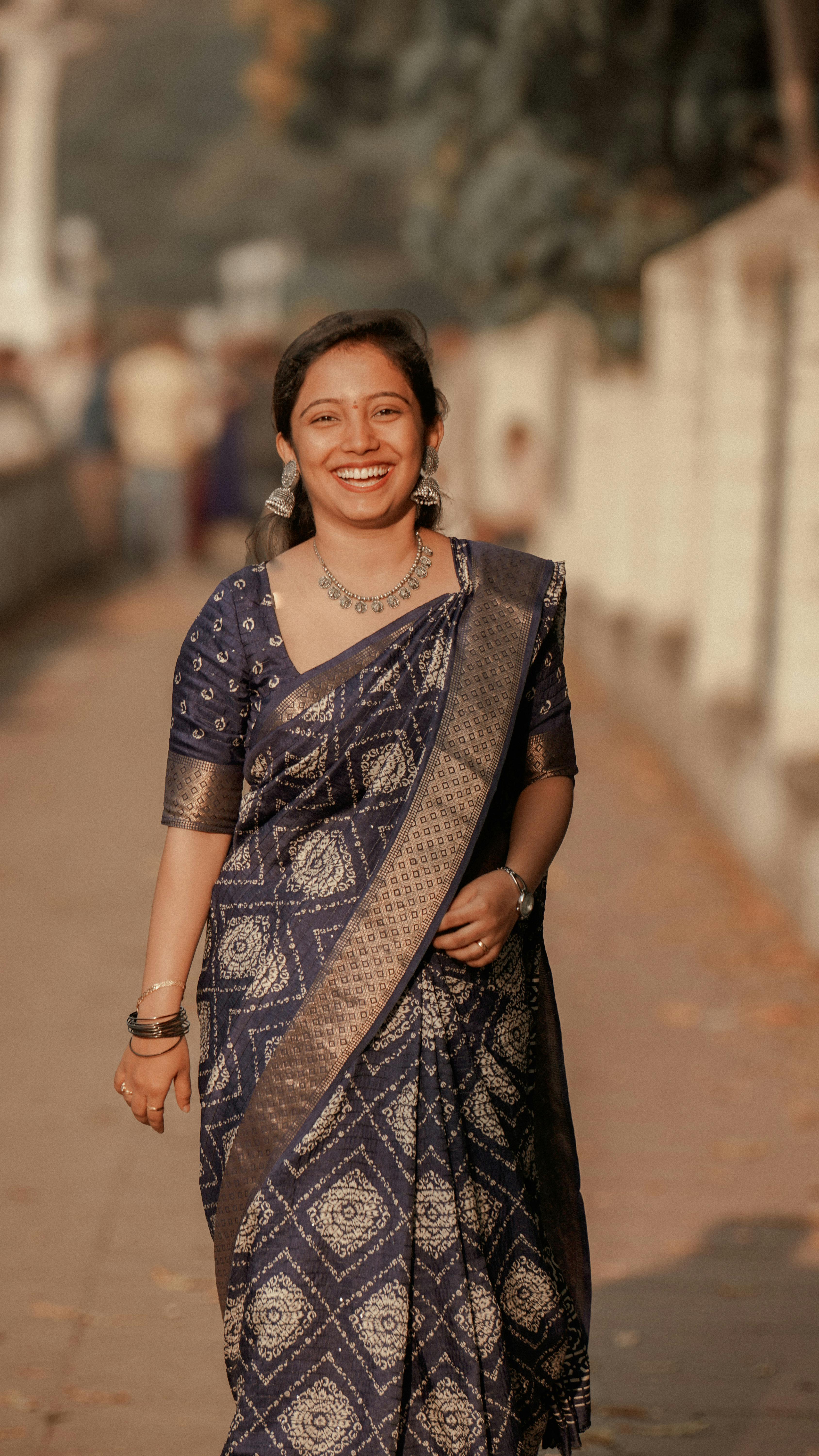 A joyful woman in a blue saree walking outdoors, exuding warmth and elegance.