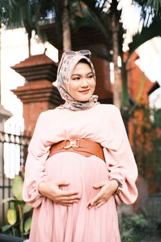 Portrait of a pregnant woman wearing a hijab, standing outdoors, embodying grace and anticipation. - Fotografer Sidoarjo