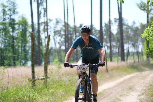 Adult cyclist riding through forest trail during sunny day mountain biking competition.