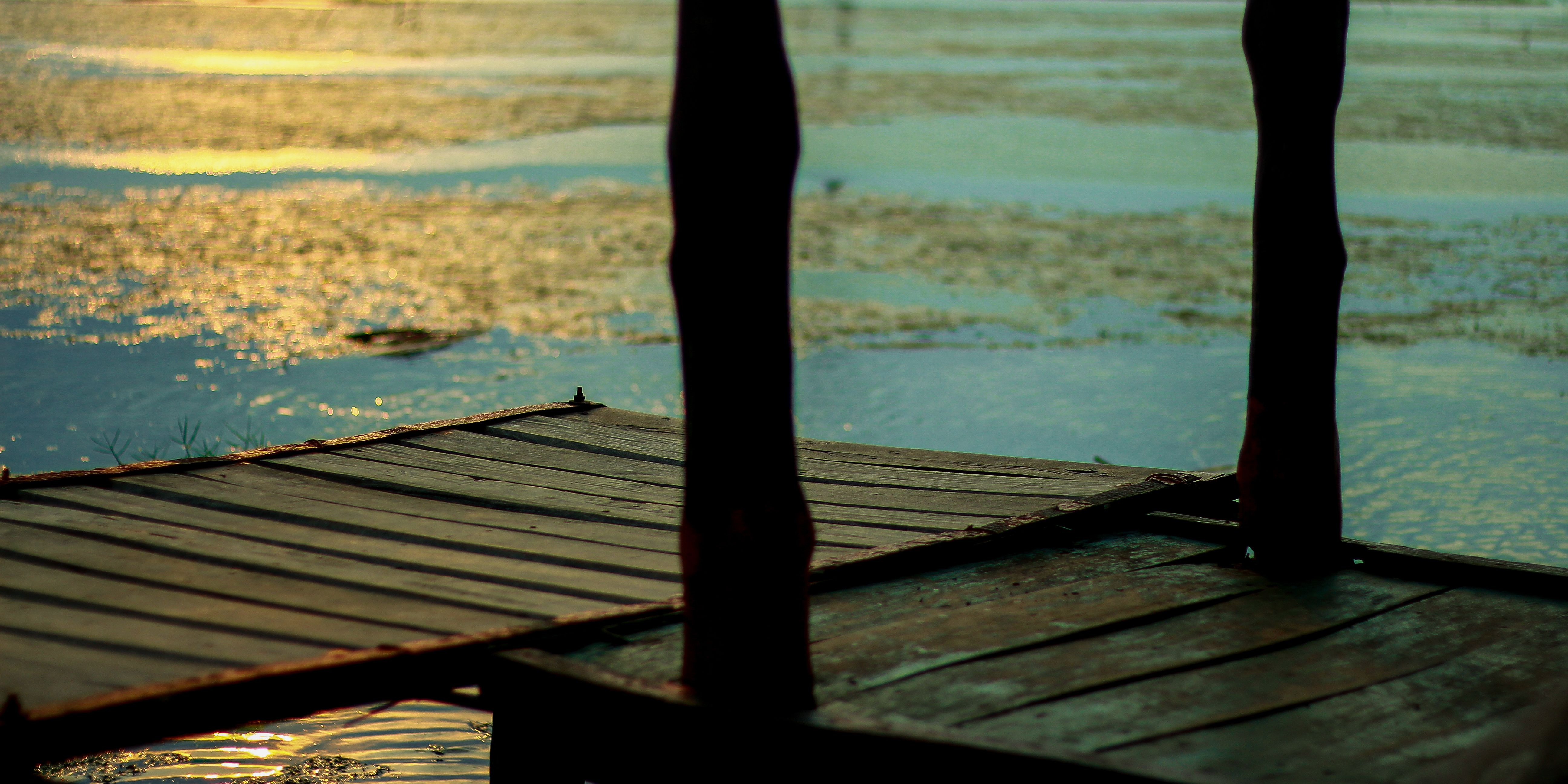 A serene sunset over a lakeside in Bangladesh with a wooden dock silhouette.