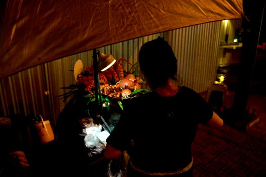 Street vendor preparing food at night under canopy lighting. Vibrant urban scene.