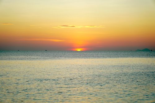 Free A tranquil ocean view at sunset with golden and orange hues painting the sky. Stock Photo