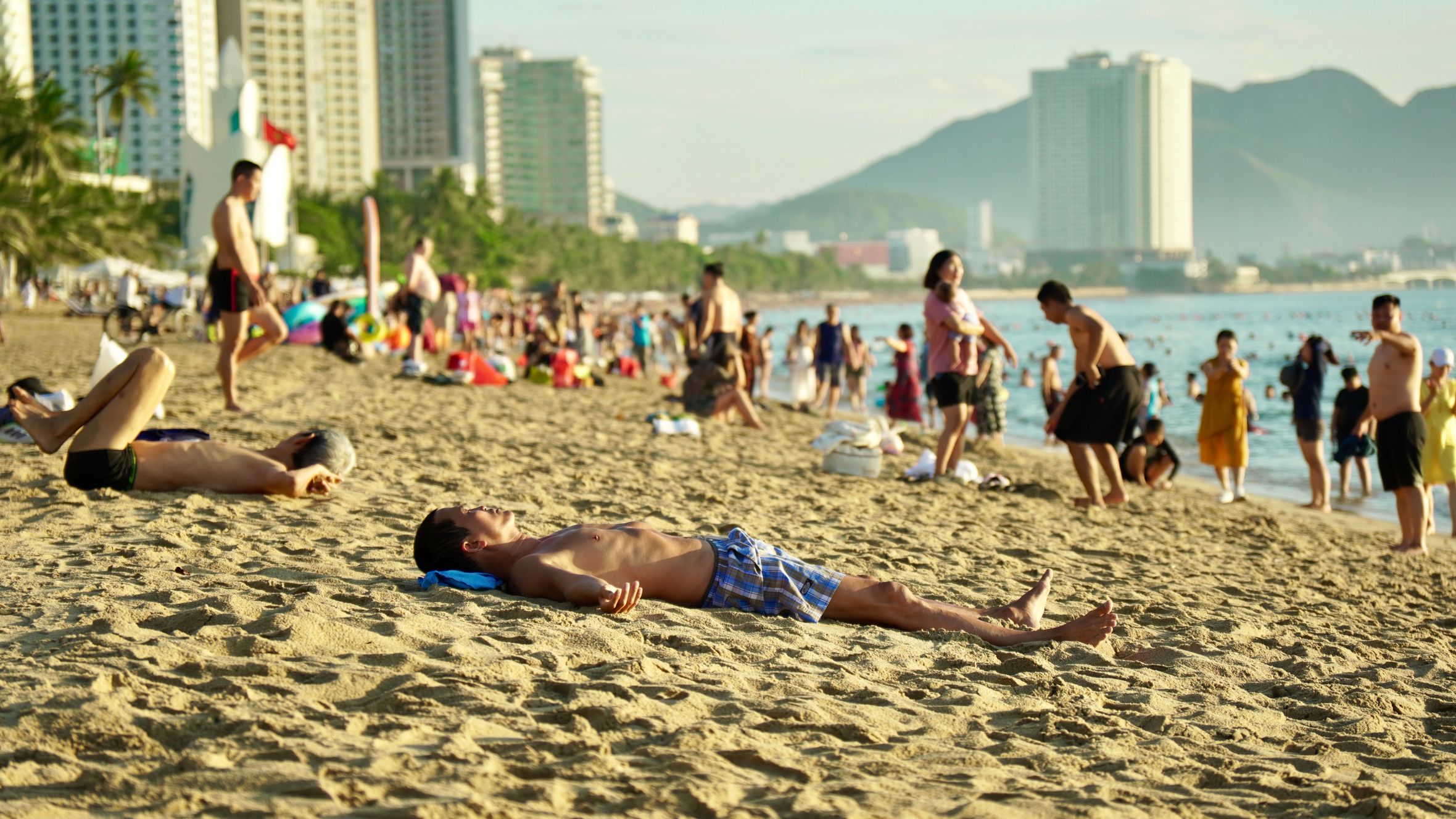 A bustling beach in Nha Trang with people sunbathing and enjoying a sunny day by the sea.