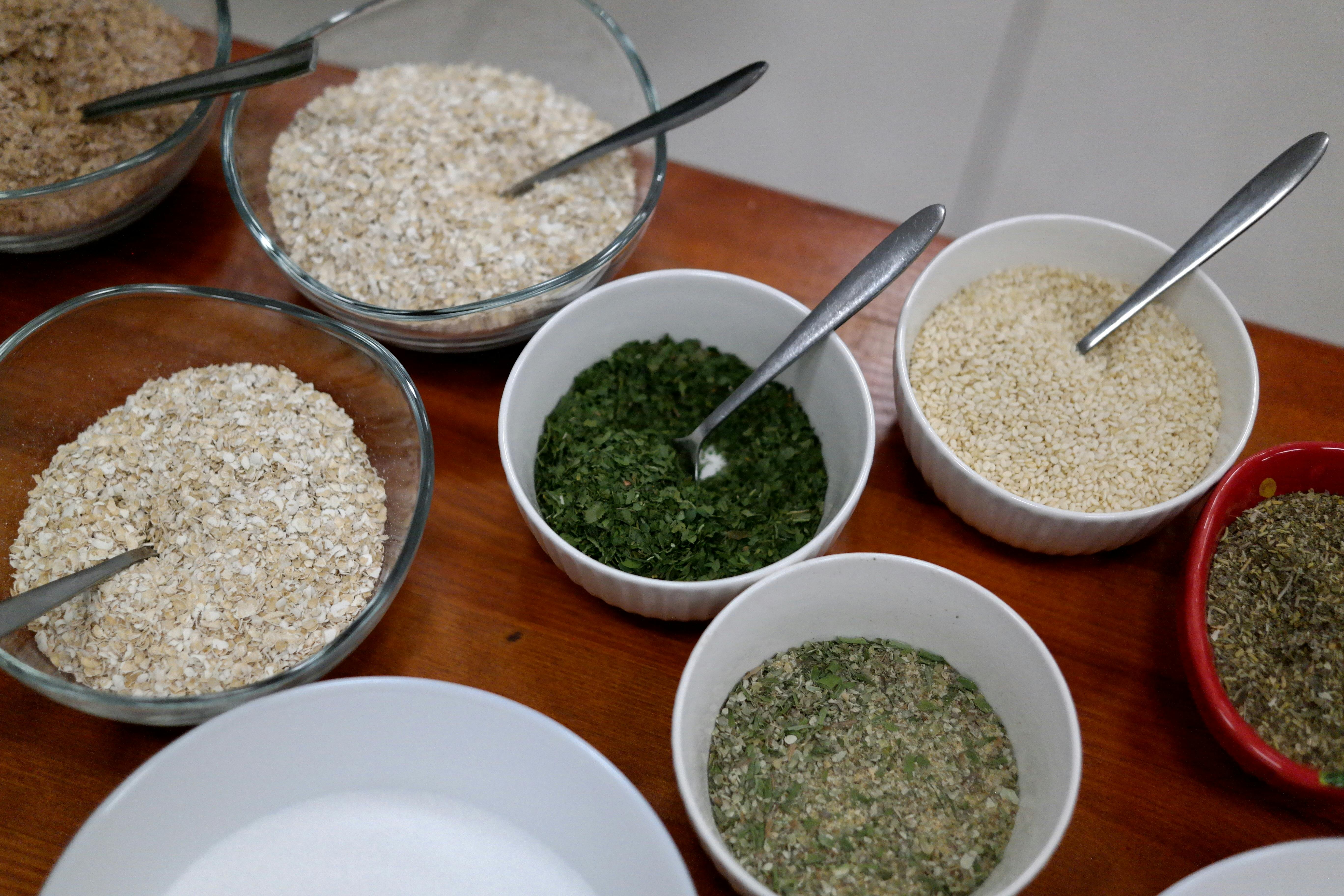 Various spices and grains in bowls with spoons on a wooden table.