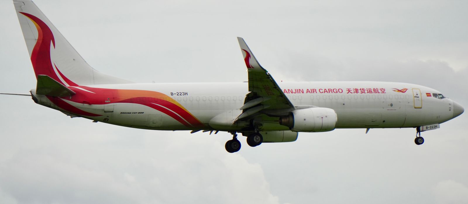 Side view of a Tianjin Air Cargo plane flying in a cloudy sky.