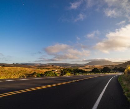 Scenic view of a winding road with golden hills and blue sky, captured at dawn.