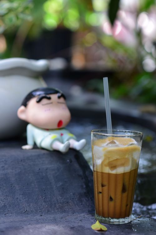 Free A glass of iced coffee beside a cartoon figurine by a water feature, outdoors. Stock Photo