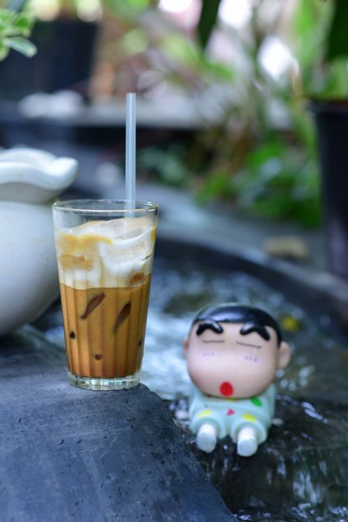 Free A refreshing glass of iced coffee with milk beside a toy figurine in a tranquil outdoor setting. Stock Photo