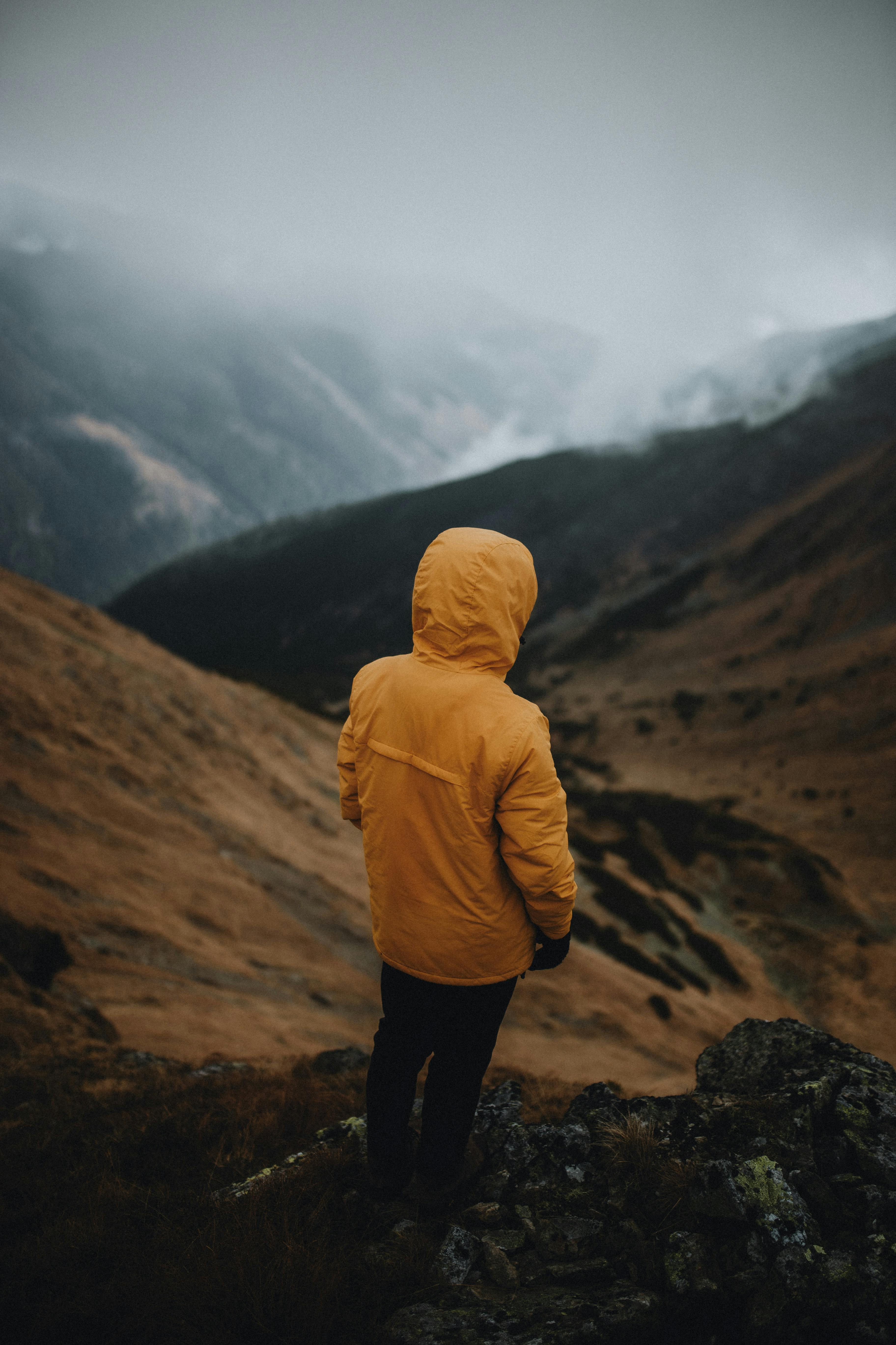 A solitary hiker in a yellow jacket gazes over the misty mountains of Vysoké Tatry, Slovakia.