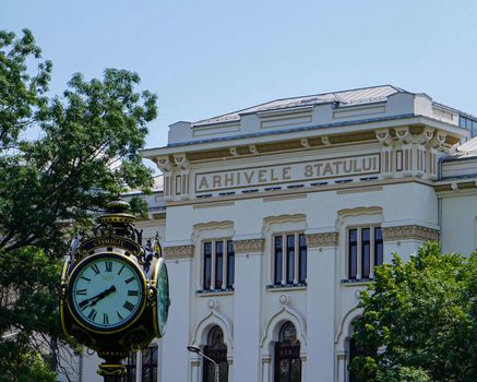 Historic building 'Arhivele Statului' with ornate street clock and greenery.