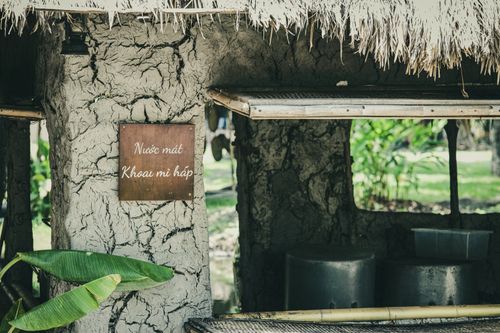 Free Outdoor setting with a clay wall and a Vietnamese sign under a thatched roof, surrounded by greenery. Stock Photo