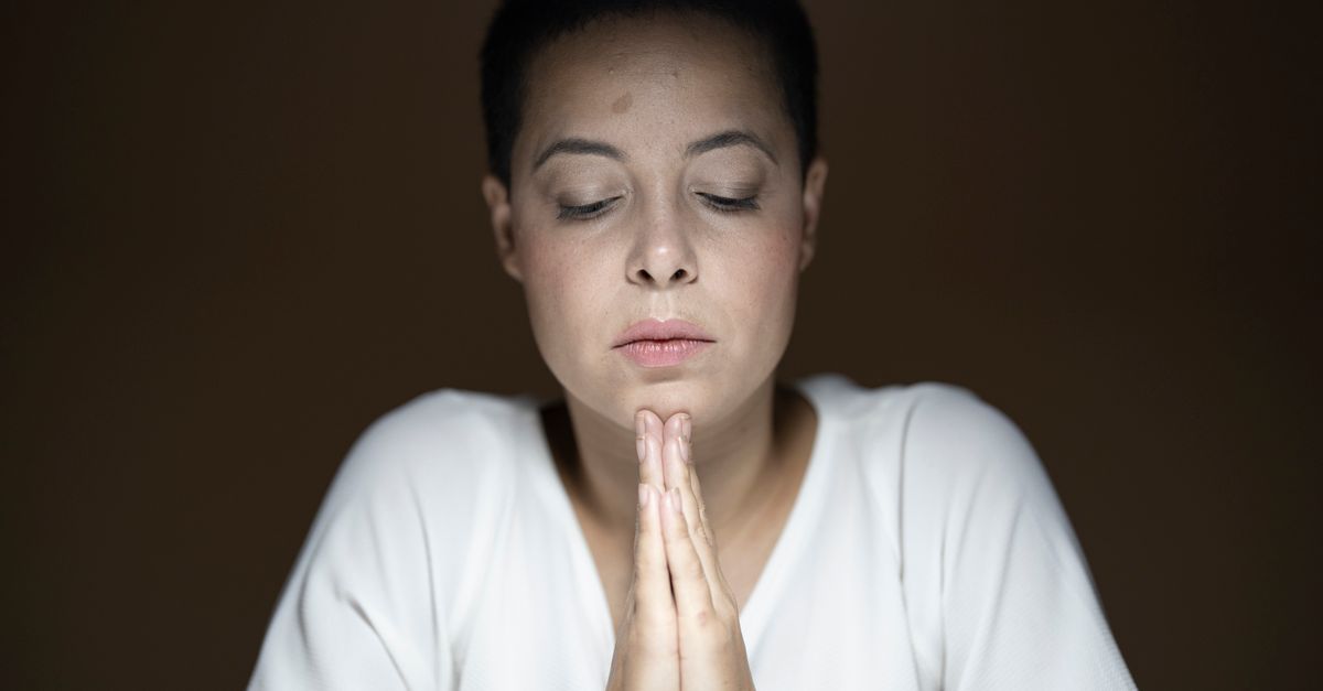 person looking out a window with hands clasped in prayer or contemplation