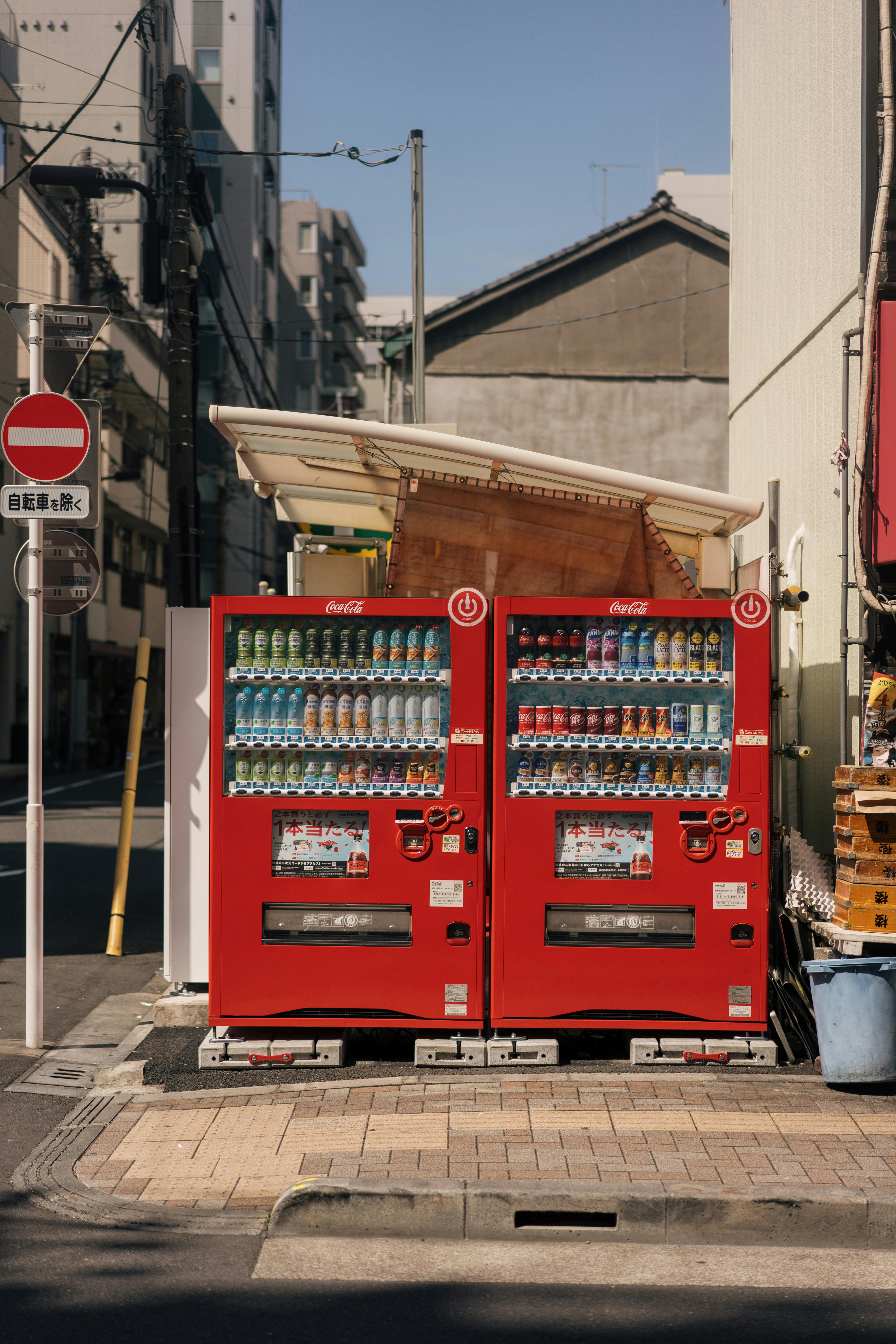 Two vending machines stand prominently on a quiet urban corner, offering a variety of beverages.