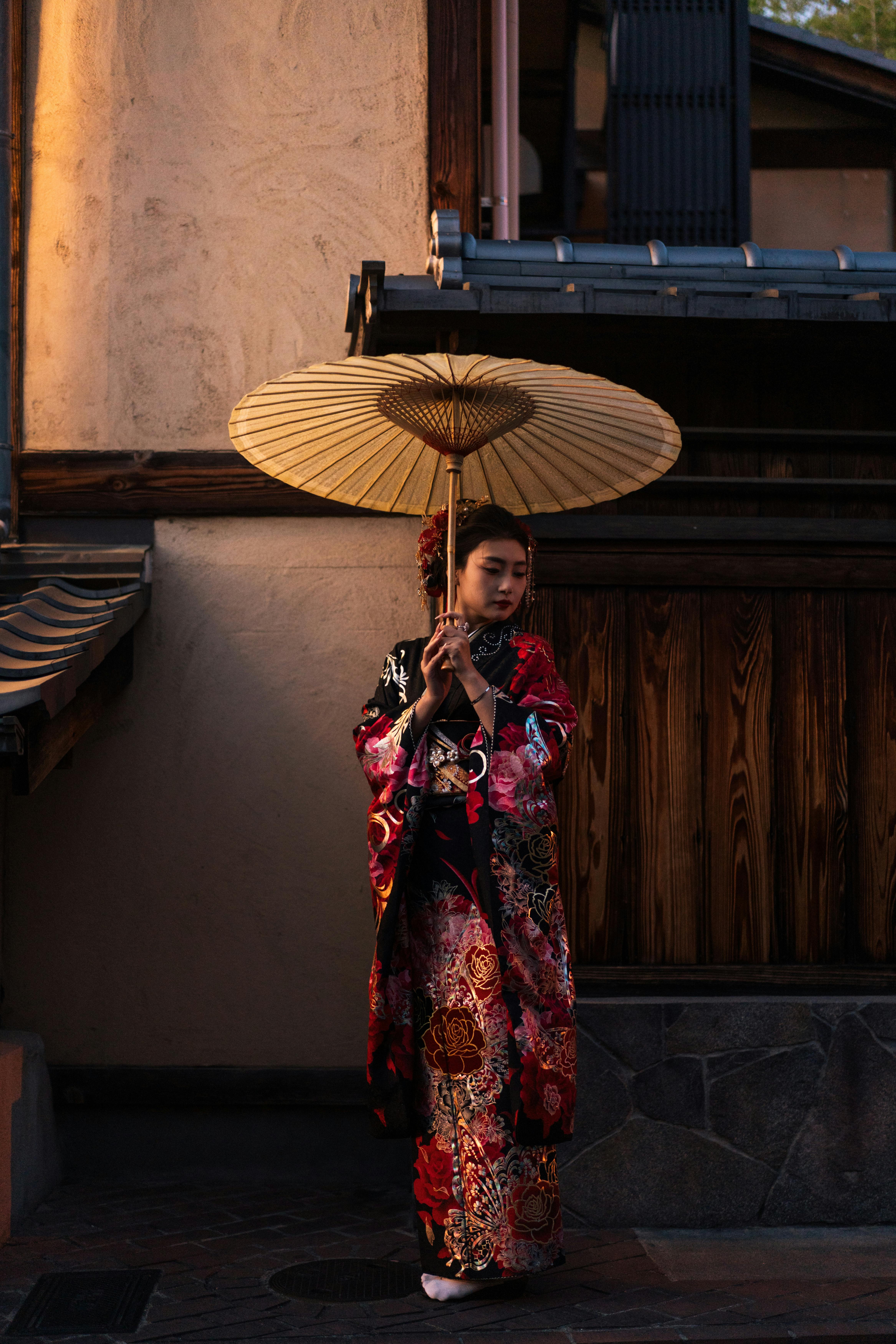 Woman in kimono under parasol, Kyoto street scene at twilight.