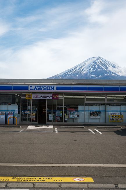 Convenience store entrance with Mount Fuji in the background under clear blue sky.