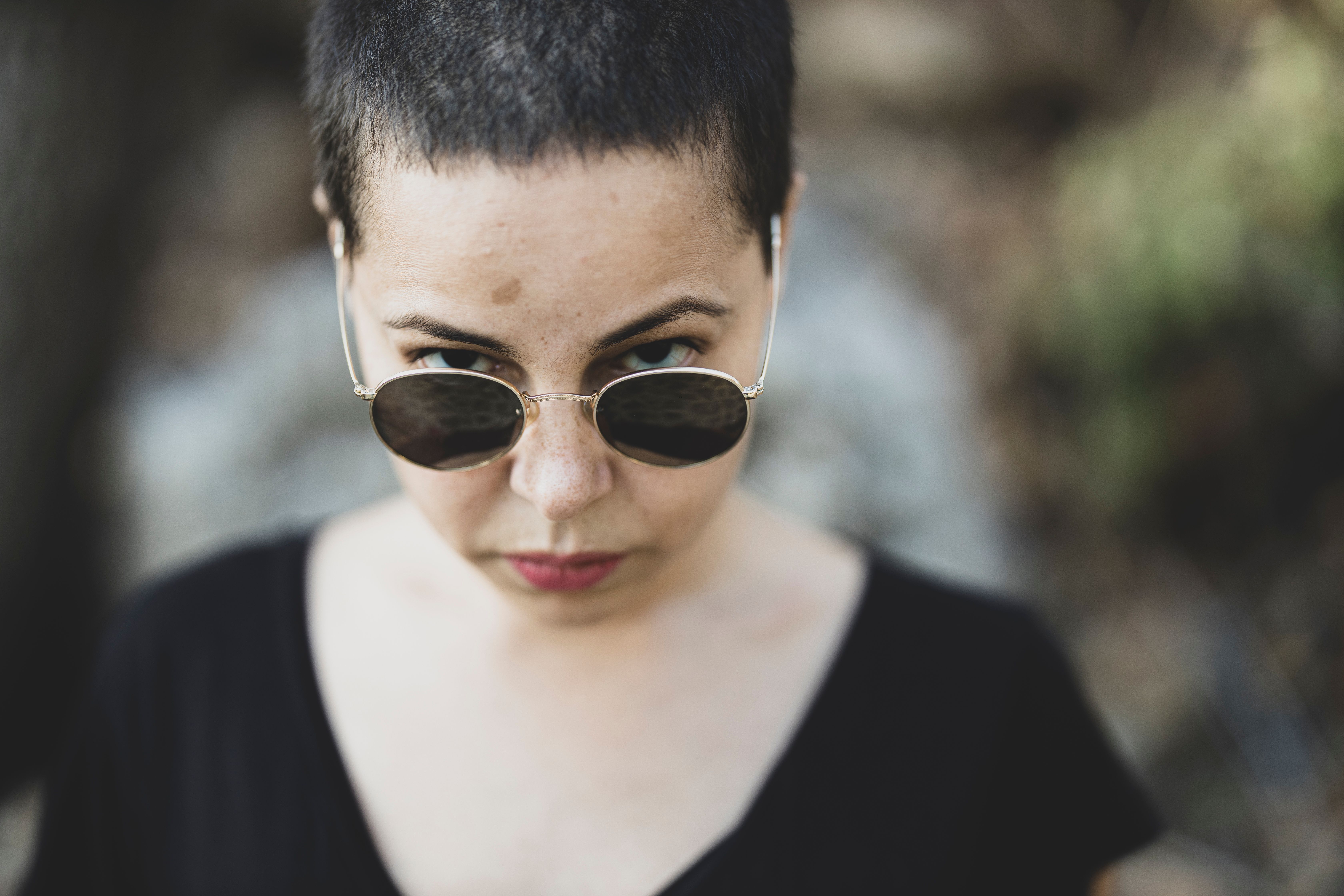 A confident woman with short hair and sunglasses gazes intensely in an outdoor setting.