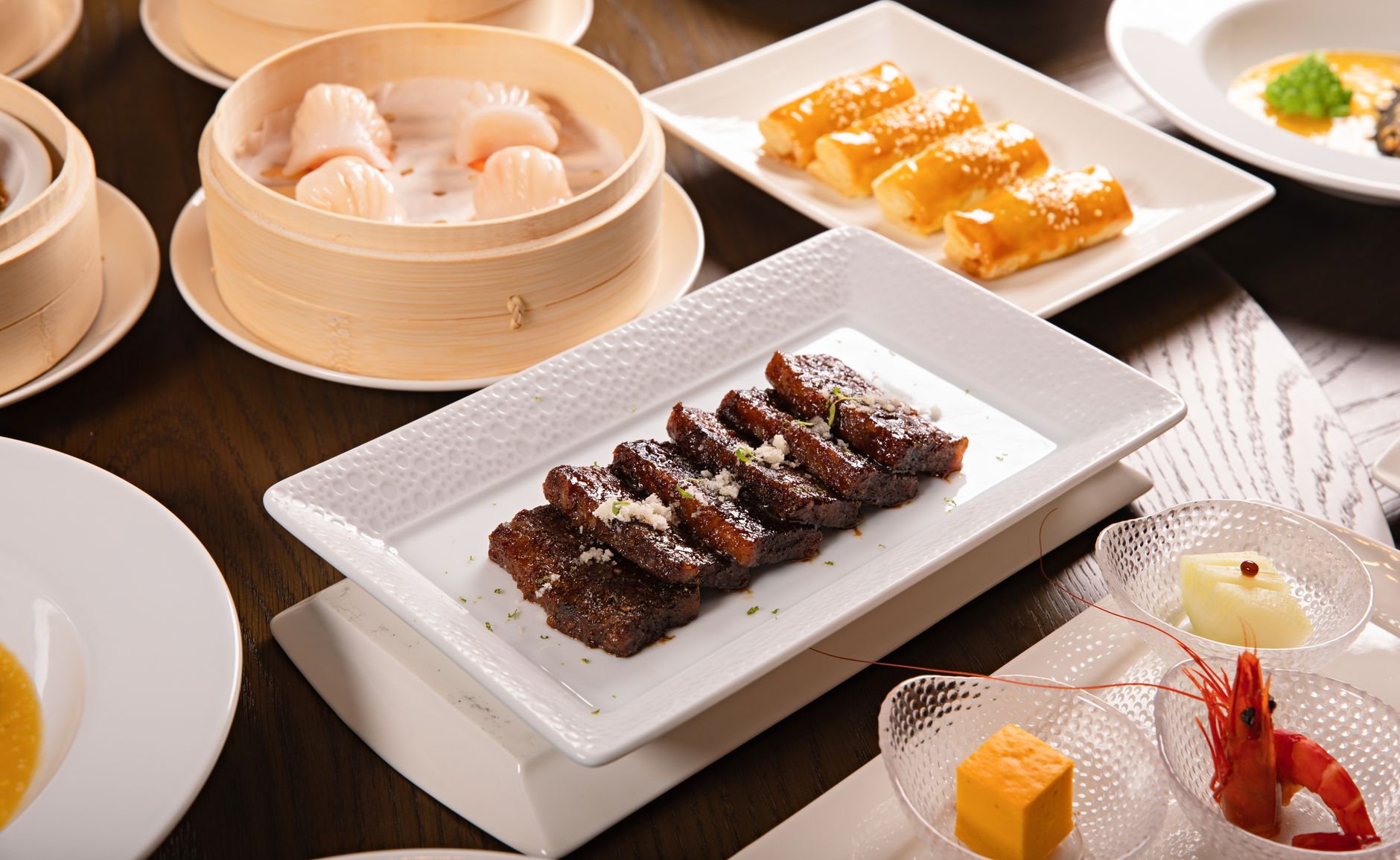 A variety of Asian dishes, including dim sum and shrimp, beautifully presented on a dining table.