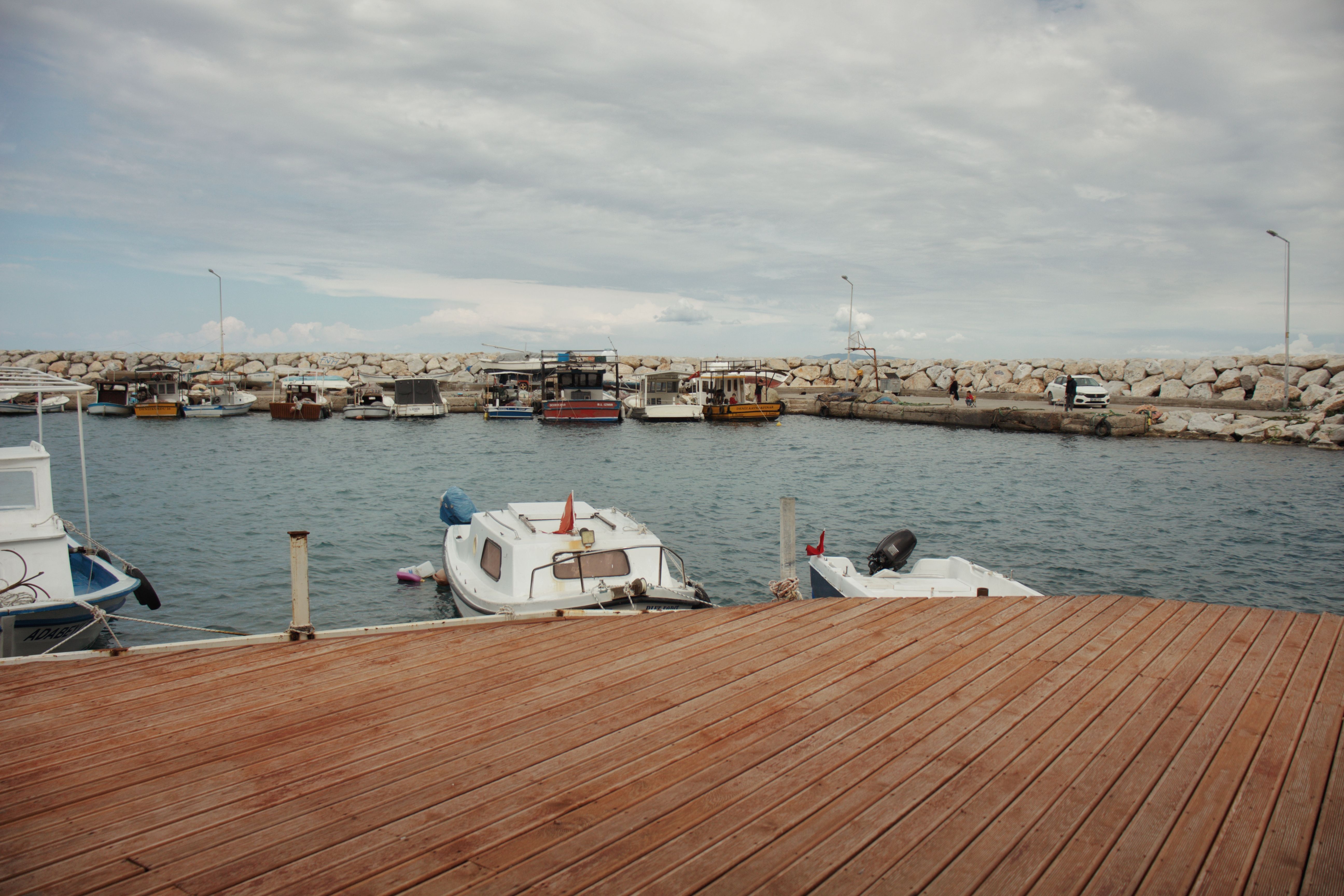 Tranquil harbor scene featuring moored boats at a wooden pier under a cloudy sky.