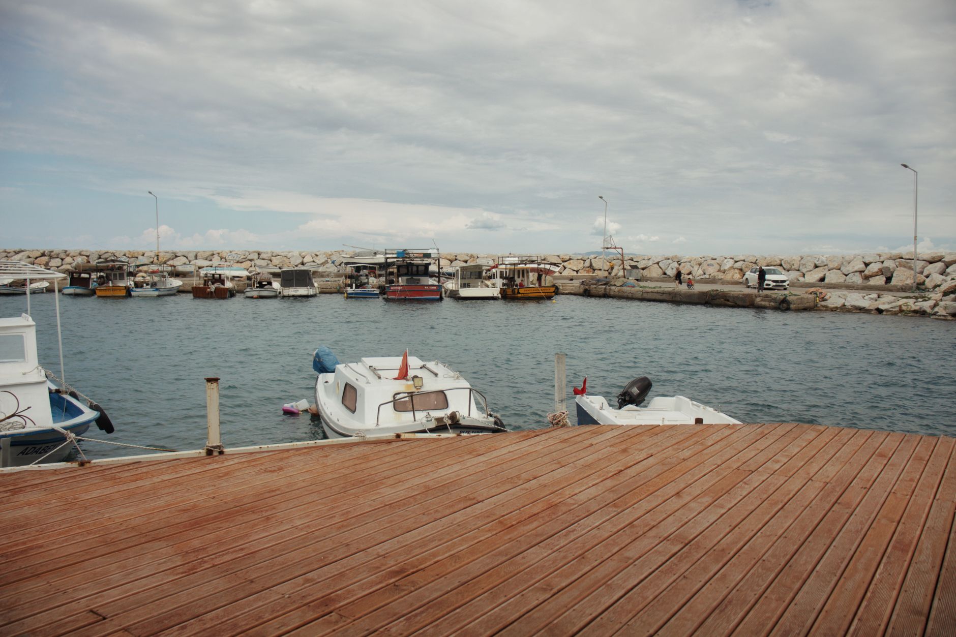 Tranquil harbor scene featuring moored boats at a wooden pier under a cloudy sky.
