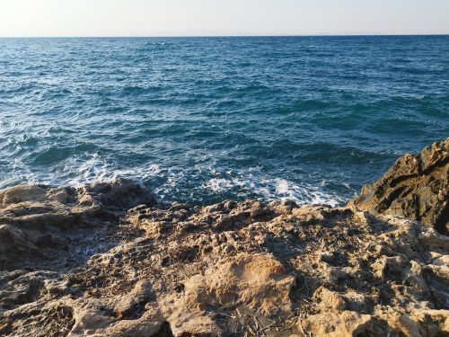 Free A scenic view of a rocky shoreline with waves crashing against the rocks and the expansive turquoise sea beyond. Stock Photo