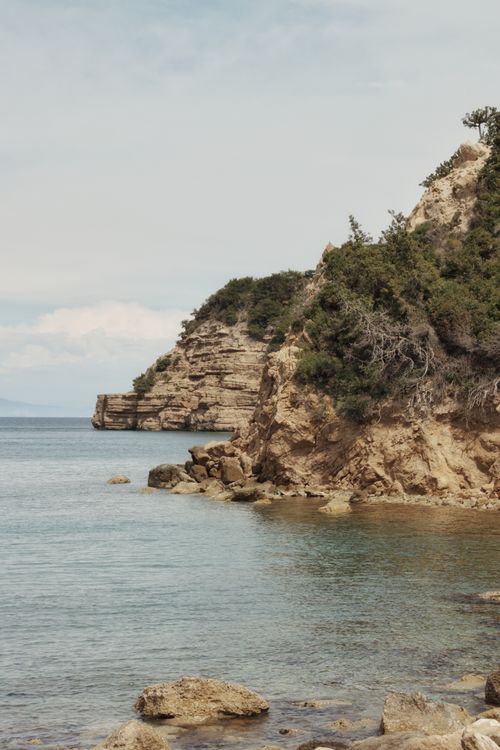 Free Tranquil coastal landscape featuring rugged cliffs and clear blue ocean under a soft sky. Stock Photo