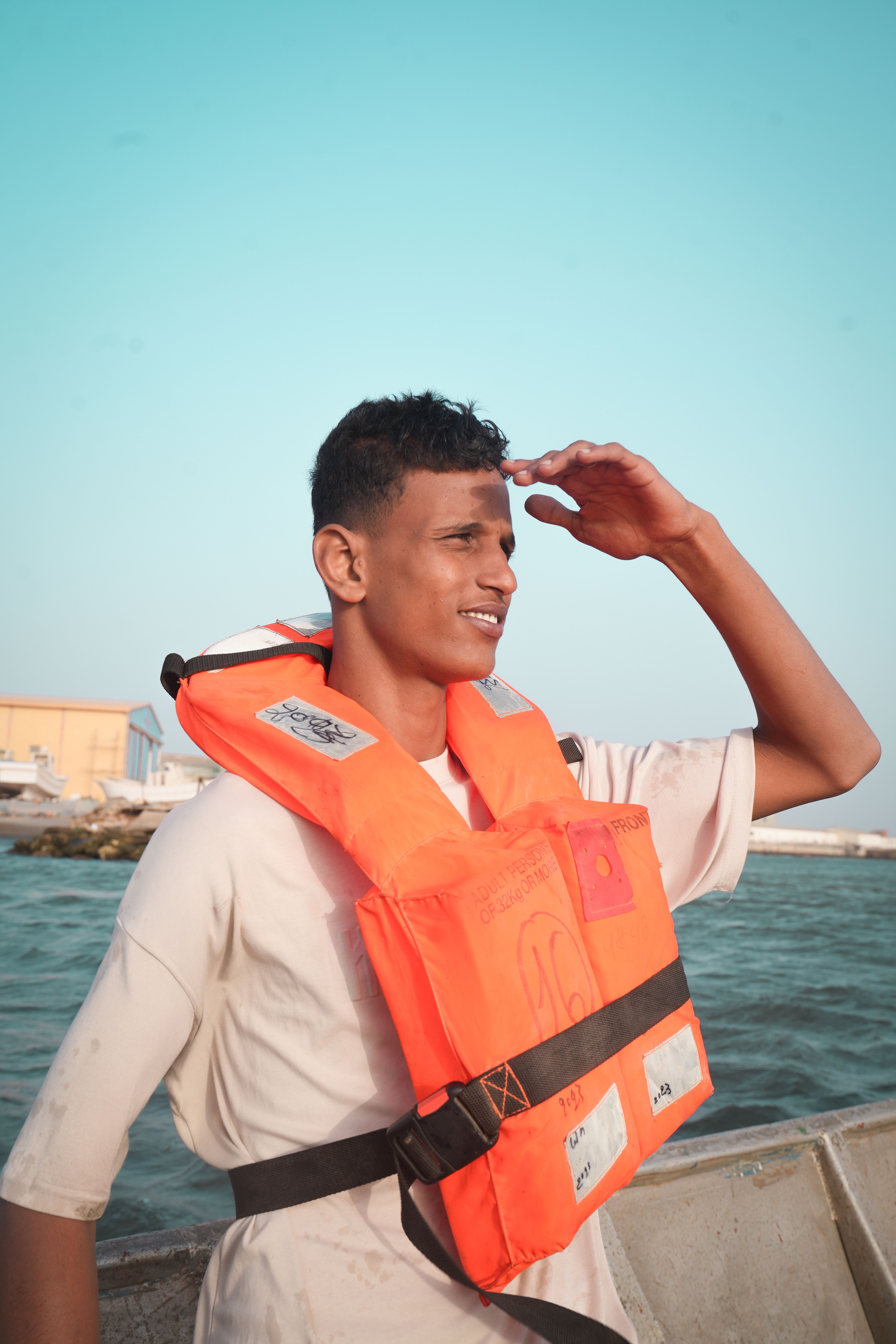 Young man with life vest looking towards horizon on a boat at sea.