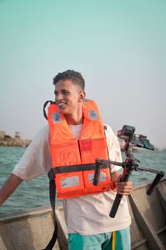 Young man with a camera stabilizer wearing a life jacket on a beach outing.