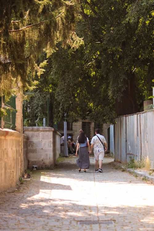 Free A couple walking hand in hand on a sunny day down a tree-lined alleyway. Stock Photo