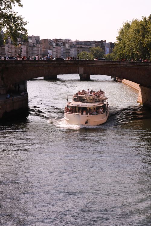 Free Tour boat cruising on the Seine River under a historic bridge in Paris, capturing a vibrant summer day. Stock Photo