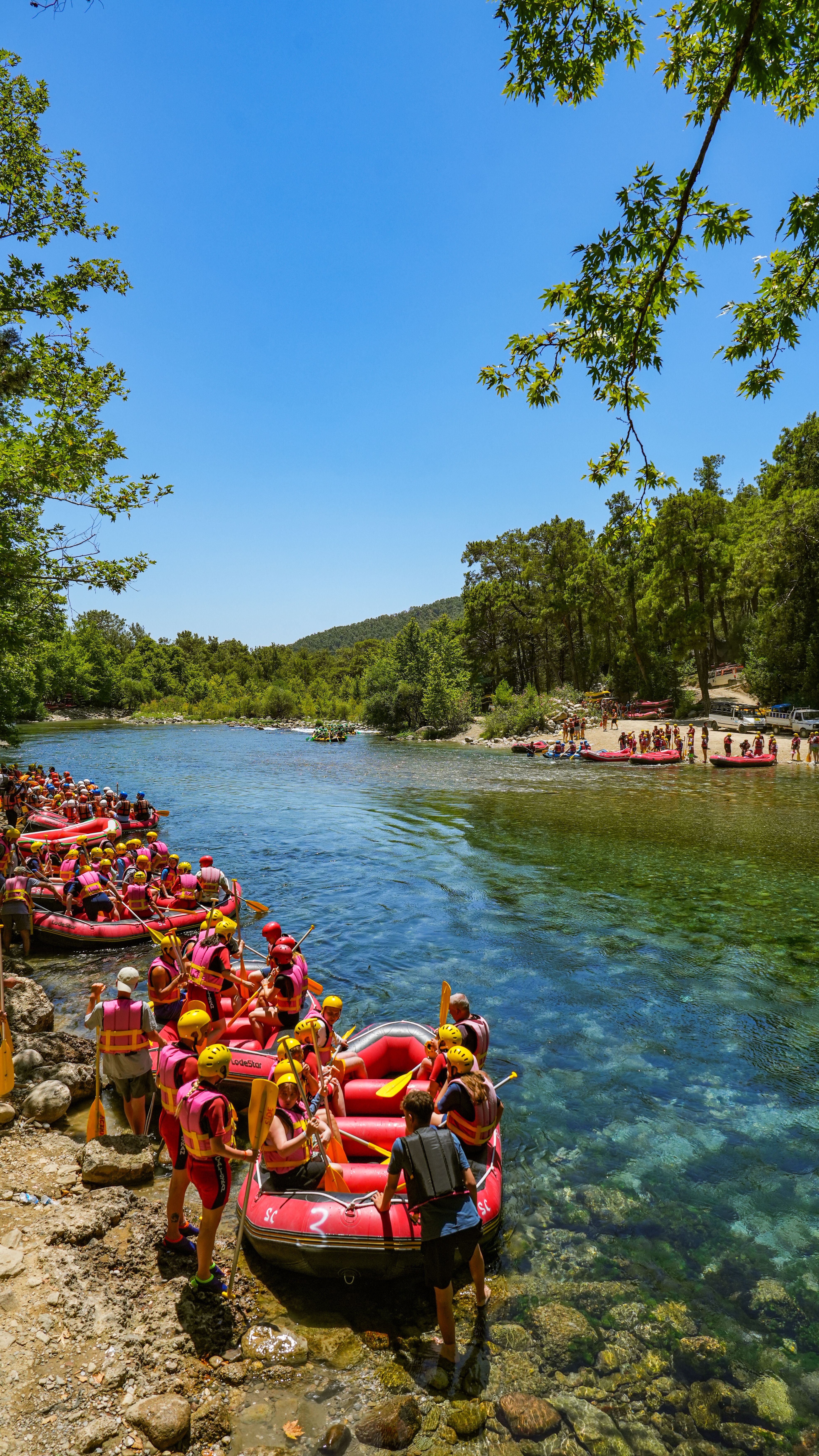 People in red rafts getting ready for river rafting under clear blue sky.