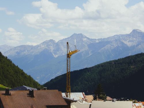 Free A construction crane amidst village rooftops with Italian Alps in the background. Stock Photo