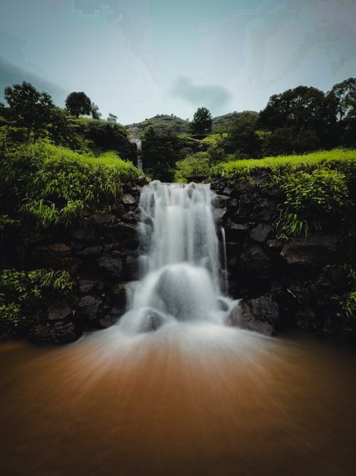 Free Picturesque waterfall cascading through vibrant greenery, capturing nature's serene beauty. Stock Photo